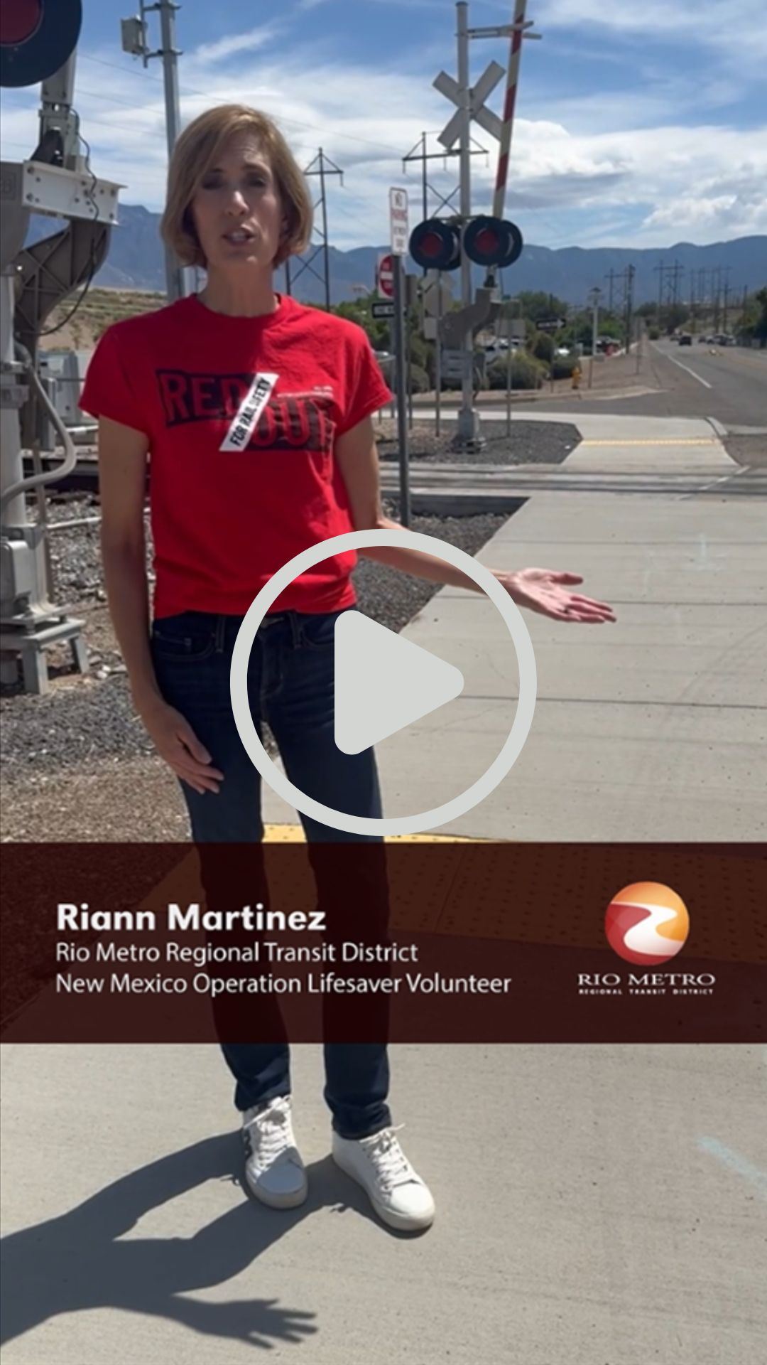 Picture of a Rio Metro employee standing near a railroad crossing and talking